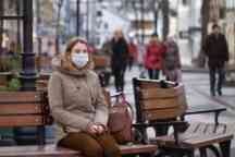 穿着棕色衣服的女人坐在长凳上，戴着口罩
