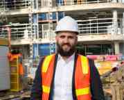 彼得·莫兰穿着安全背心和安全帽站在建筑工地前的照片。