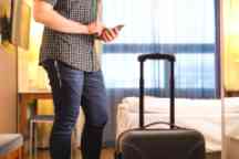 在酒店房间里拿着行李和行李箱使用智能手机的男人。游客在假日租赁公寓用手机。叫出租车或在线办理登记手续。