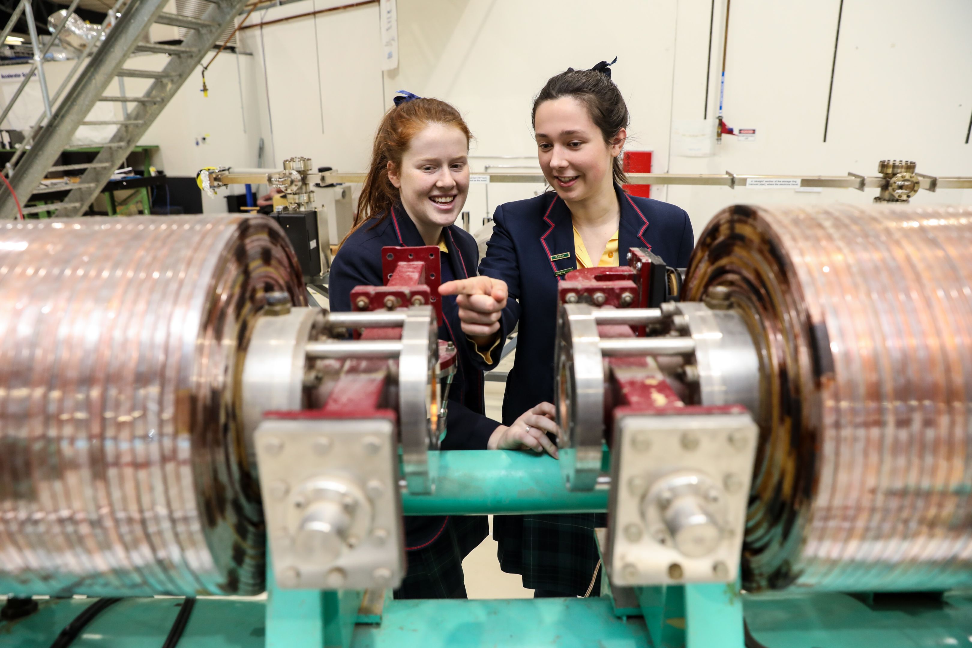 Two students on a synchrotron school tour. 两个微笑的女高中生正在检查一台同步加速器