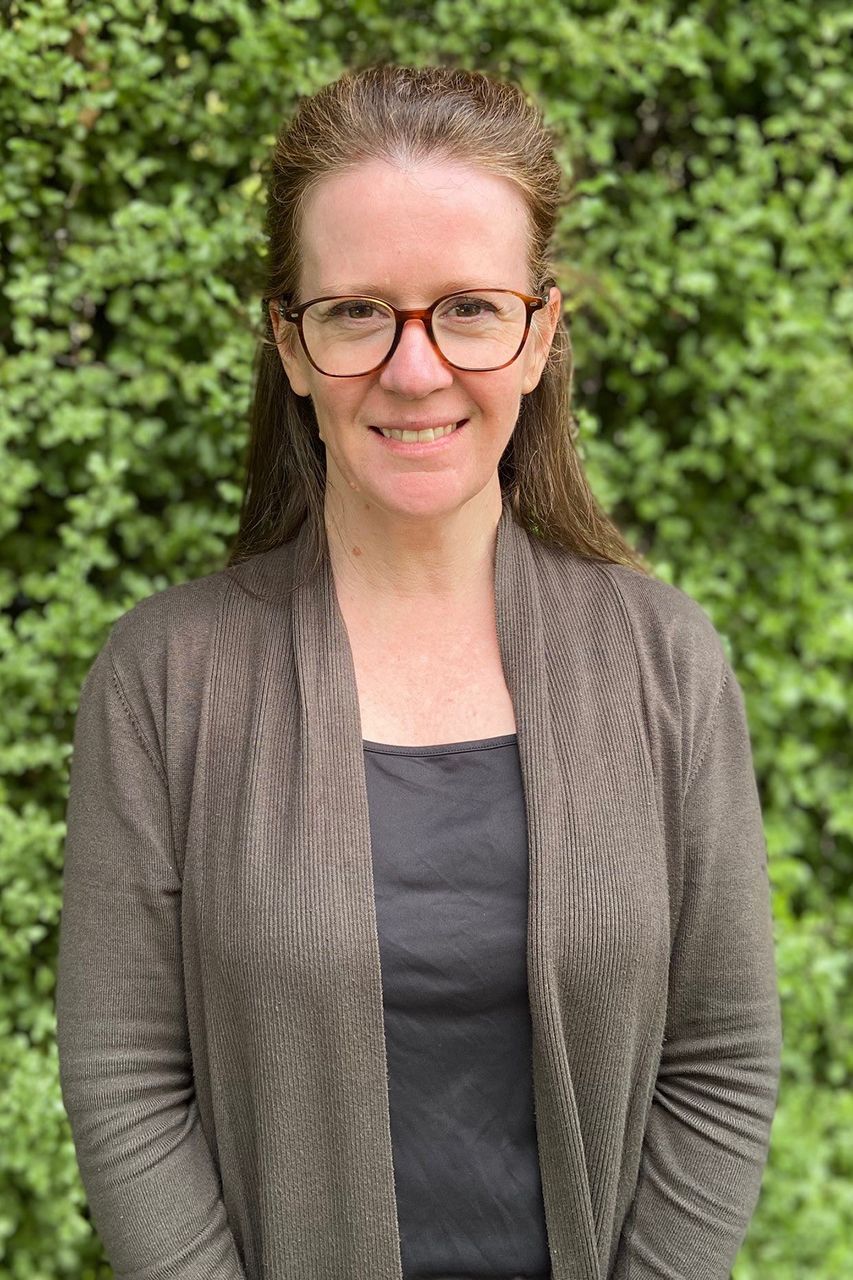 Narelle Caulfield 纳勒尔留着棕色长发,戴着眼镜,穿着一件棕色开衫。