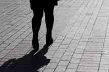 孤独女人的剪影走在街上，人行道上的黑影