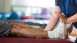 一位女职业治疗师抱着一位脚踝缠着绷带的男病人的腿和脚。