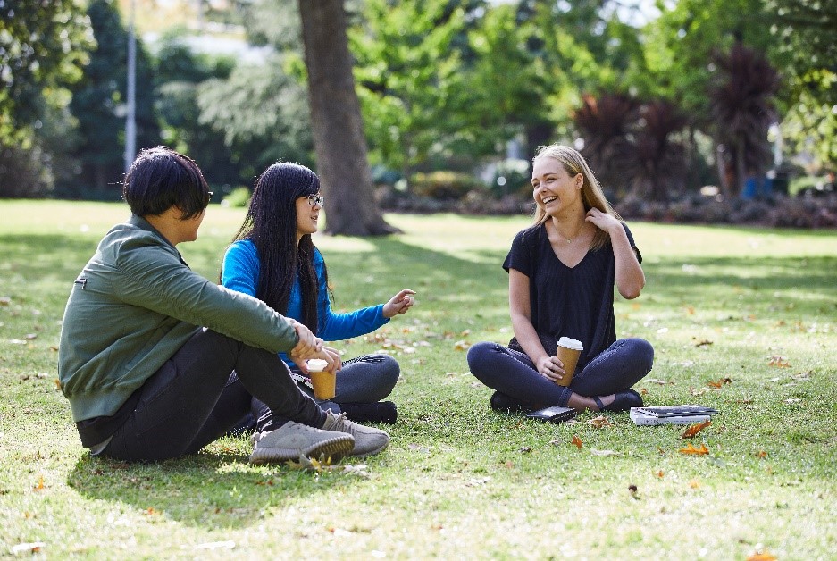 三个学生坐在公园里边喝咖啡边笑