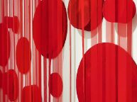 一系列不同大小的红色泡沫圆圈分布在白色的墙壁上，上面覆盖着布条帘子