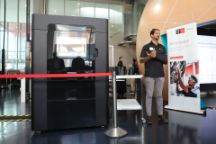 一台巨大的黑色3D打印机站在一名演示人员的旁边