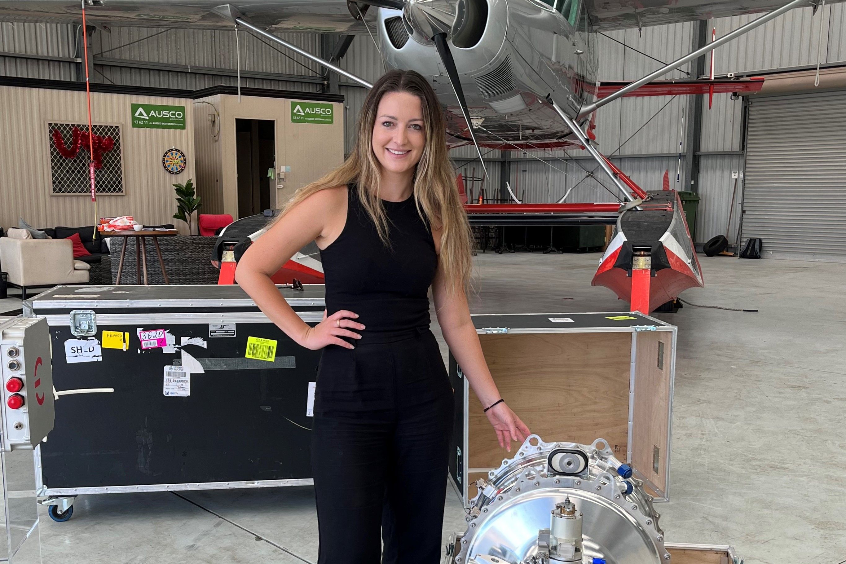 一名女子站在飞机的衣架上，身后是一架小飞机，旁边是飞机引擎。