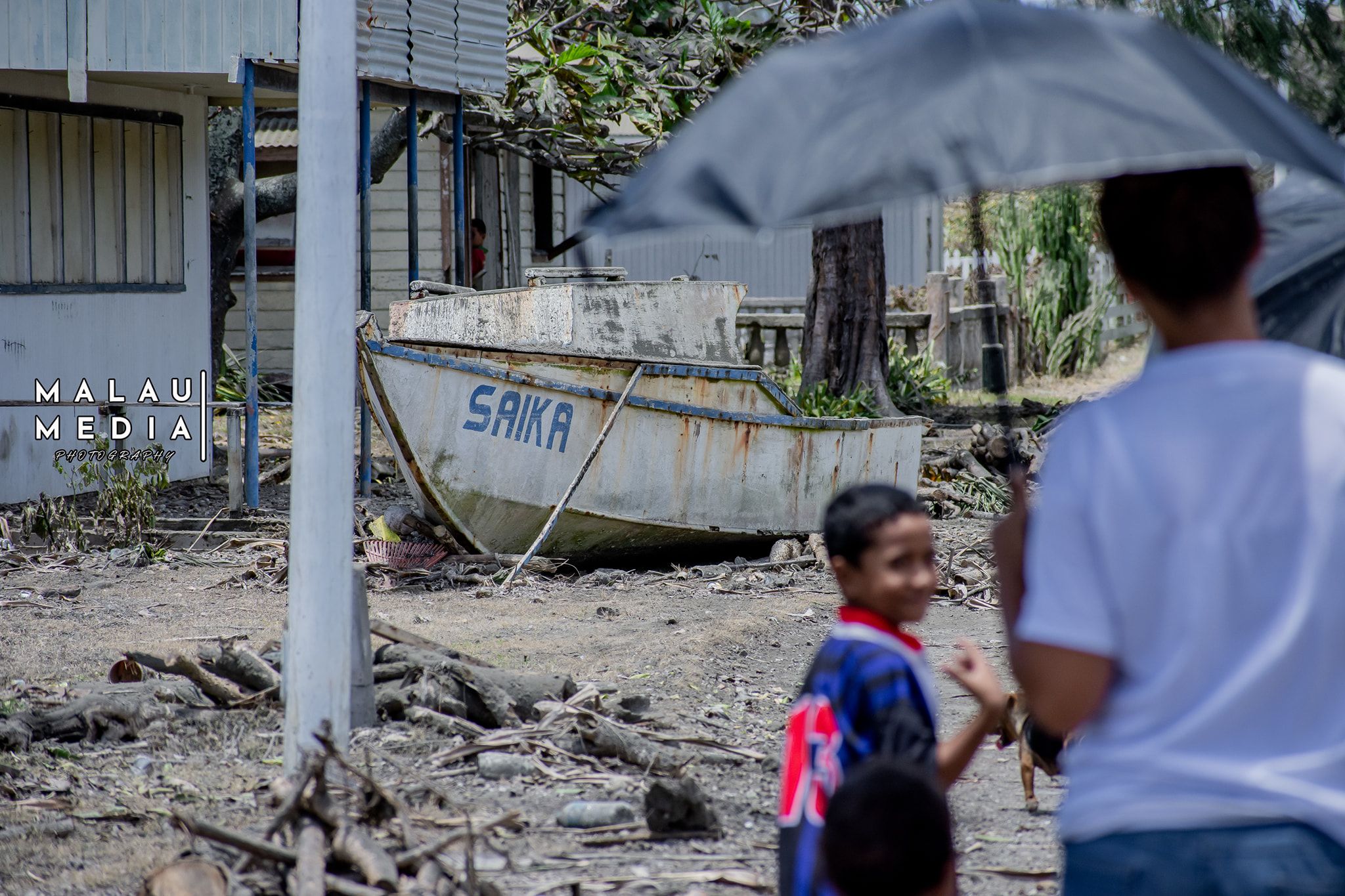 2022年1月，两个汤加人在观察海啸造成的破坏，一个小孩和一个成年人打着伞