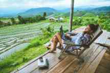 亚洲女性旅游自然。旅行放松。坐在度假村的阳台上用笔记本电脑工作。夏天山上的田野。泰国