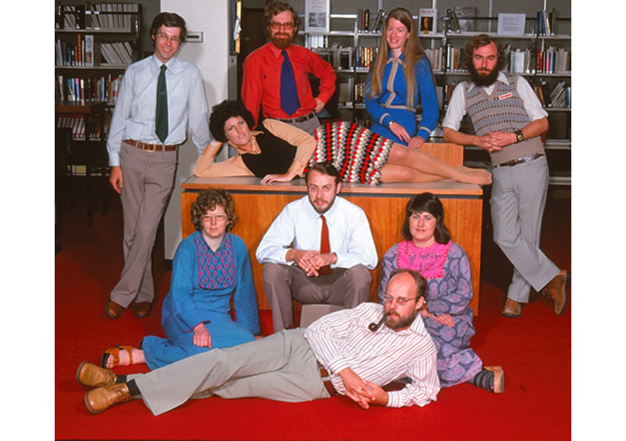 1974年，9名图书馆员在史文朋图书馆合影留念。他们穿着典型的20世纪70年代的衣服——涡纹花呢、木屐和钩针。一个躺在桌子对面，另一个躺在前面抽烟斗!