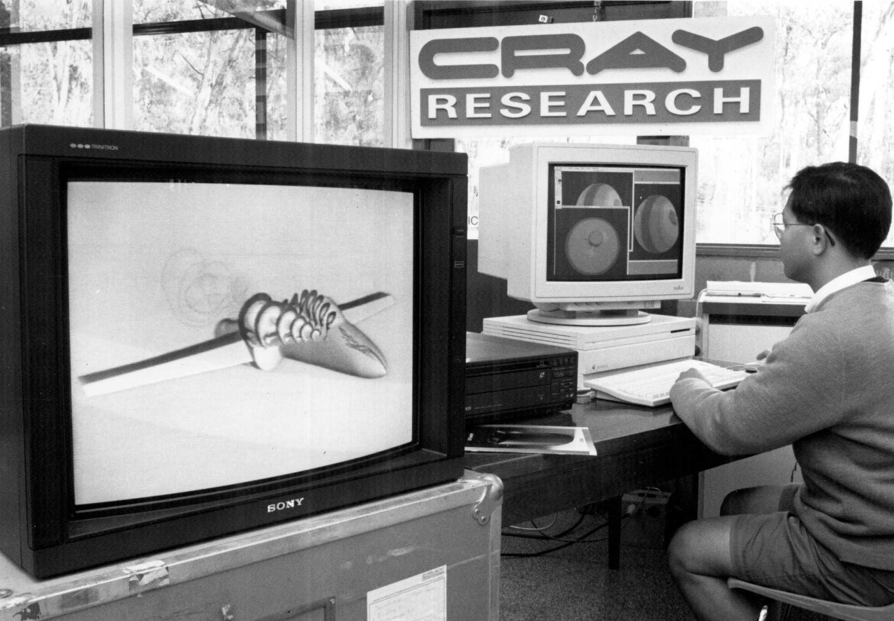 一张黑白照片，一个男人坐在一台90年代风格的电脑前。他正在看屏幕上的图形