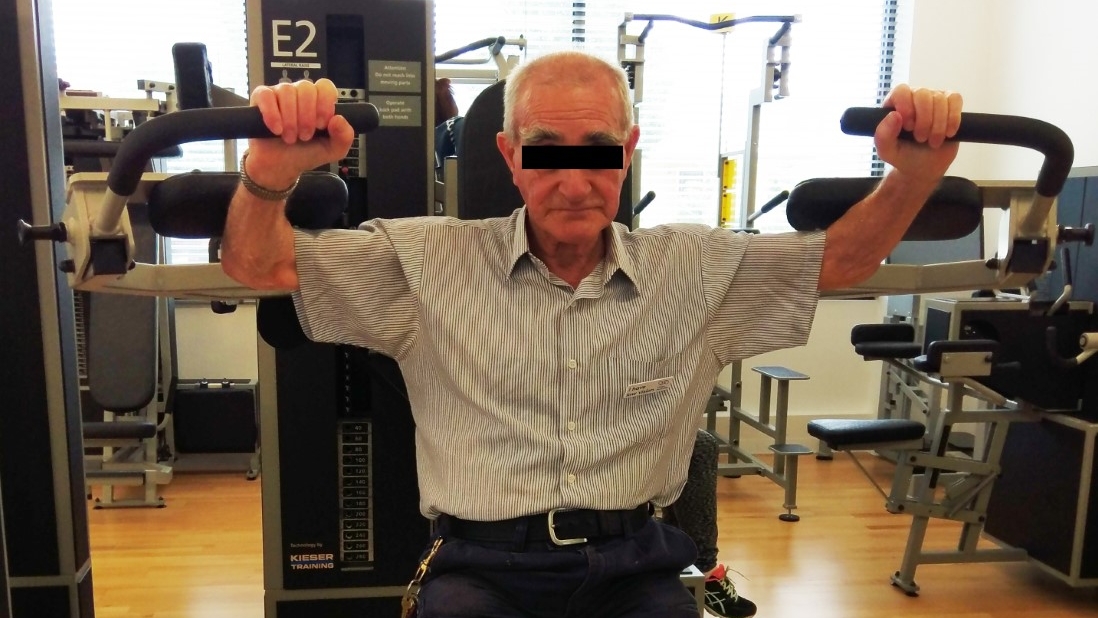 图为，一位上了年纪的男性正在健身房的健身器材上做仰卧起坐