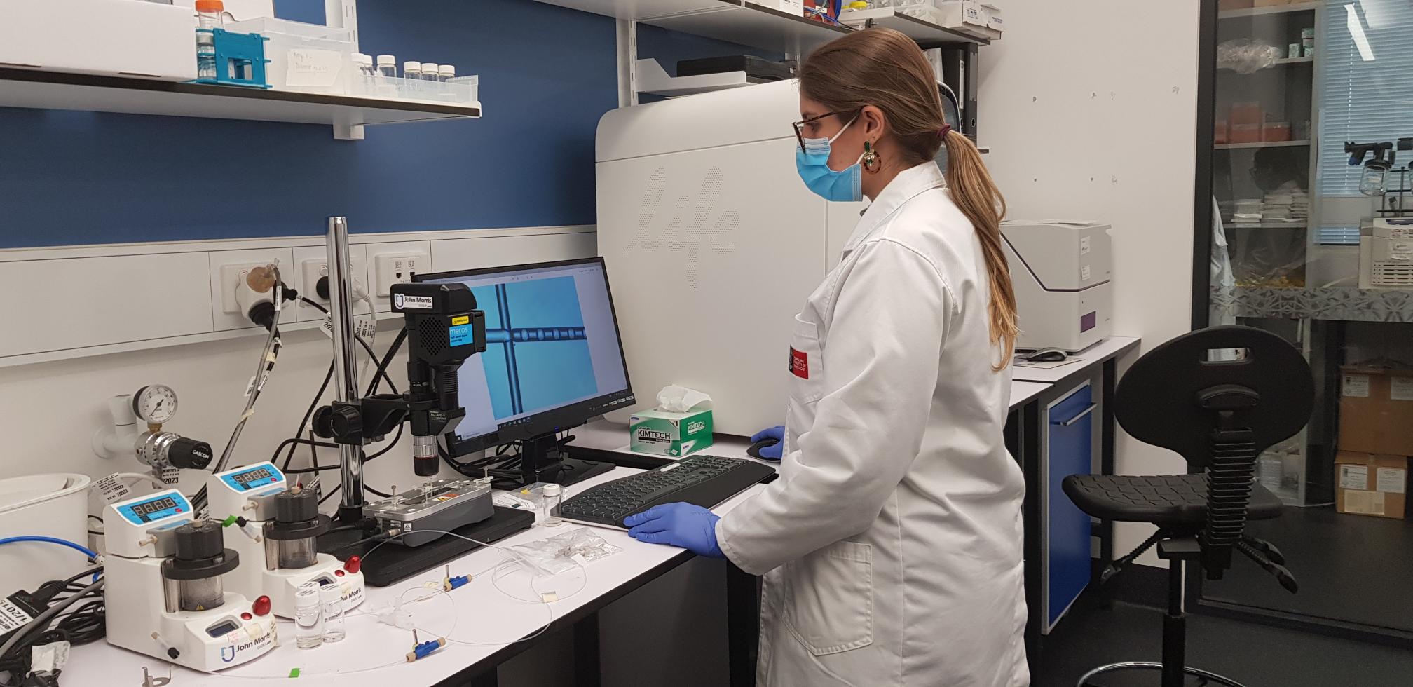 一名身穿实验服、戴着口罩的研究人员在BioFab3D实验室的计算机上工作