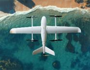 一架白色无人驾驶飞机在水面和海滩上空飞行