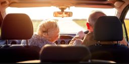 一对老夫妇在一辆车里，男人在右边开车，女人坐在左边的副驾驶座位上。阳光透过前车窗刺眼地照进来。镜头是从后排中间的副驾驶位置拍摄的。