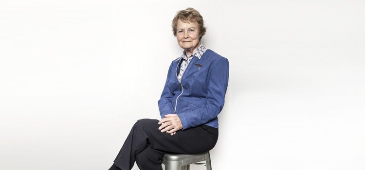 一个年长的女人穿着蓝色上衣和黑色裤子坐在凳子上放松的姿势