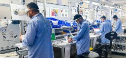 科学家们穿着蓝色的实验室大褂，戴着口罩，戴着屏幕保护罩，在一个被机器包围的实验室里工作