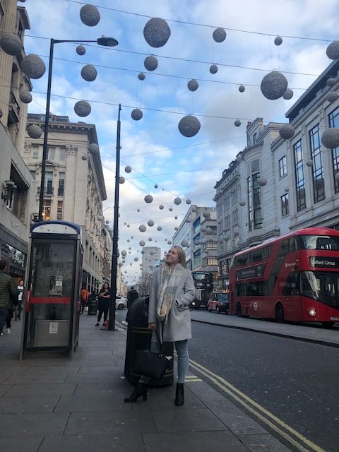 一位女士站在繁忙的伦敦街道上，头顶上装饰着圣诞装饰品