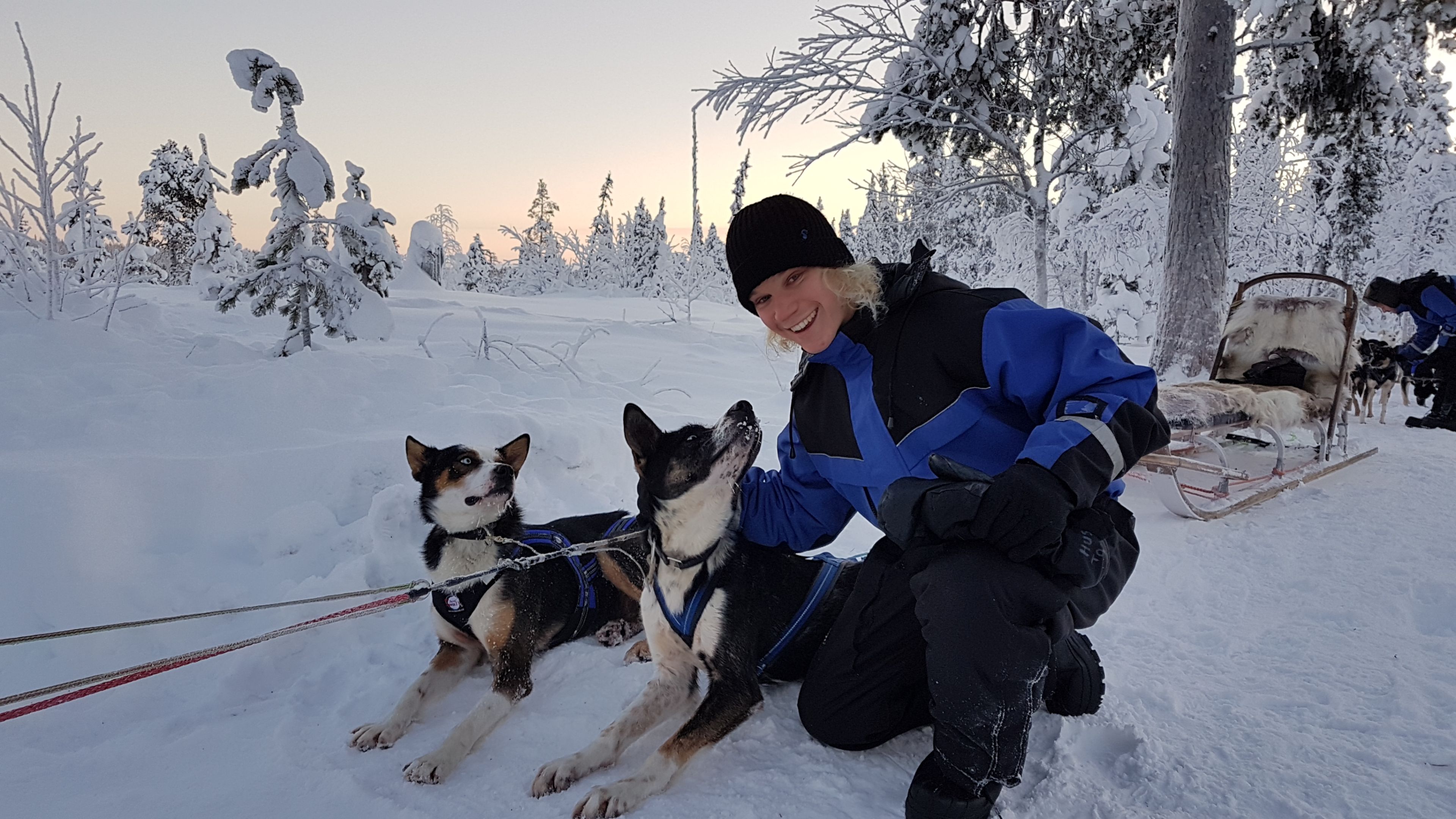 一名留学瑞典的学生对着镜头微笑，背景是一只狗拉的雪橇