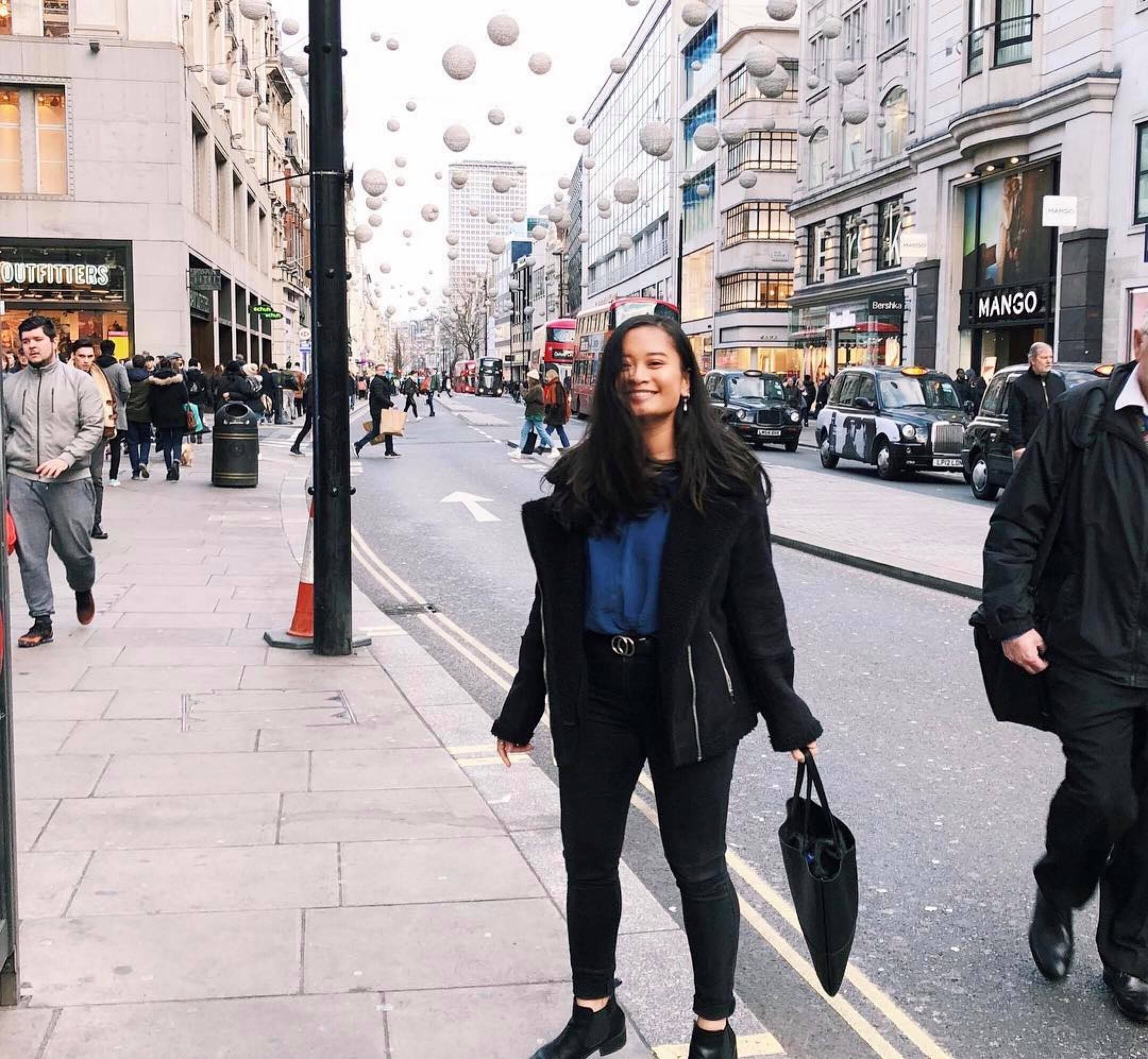 出国留学学生穿着黑裤子和夹克,繁忙的伦敦大街上对着镜头微笑
