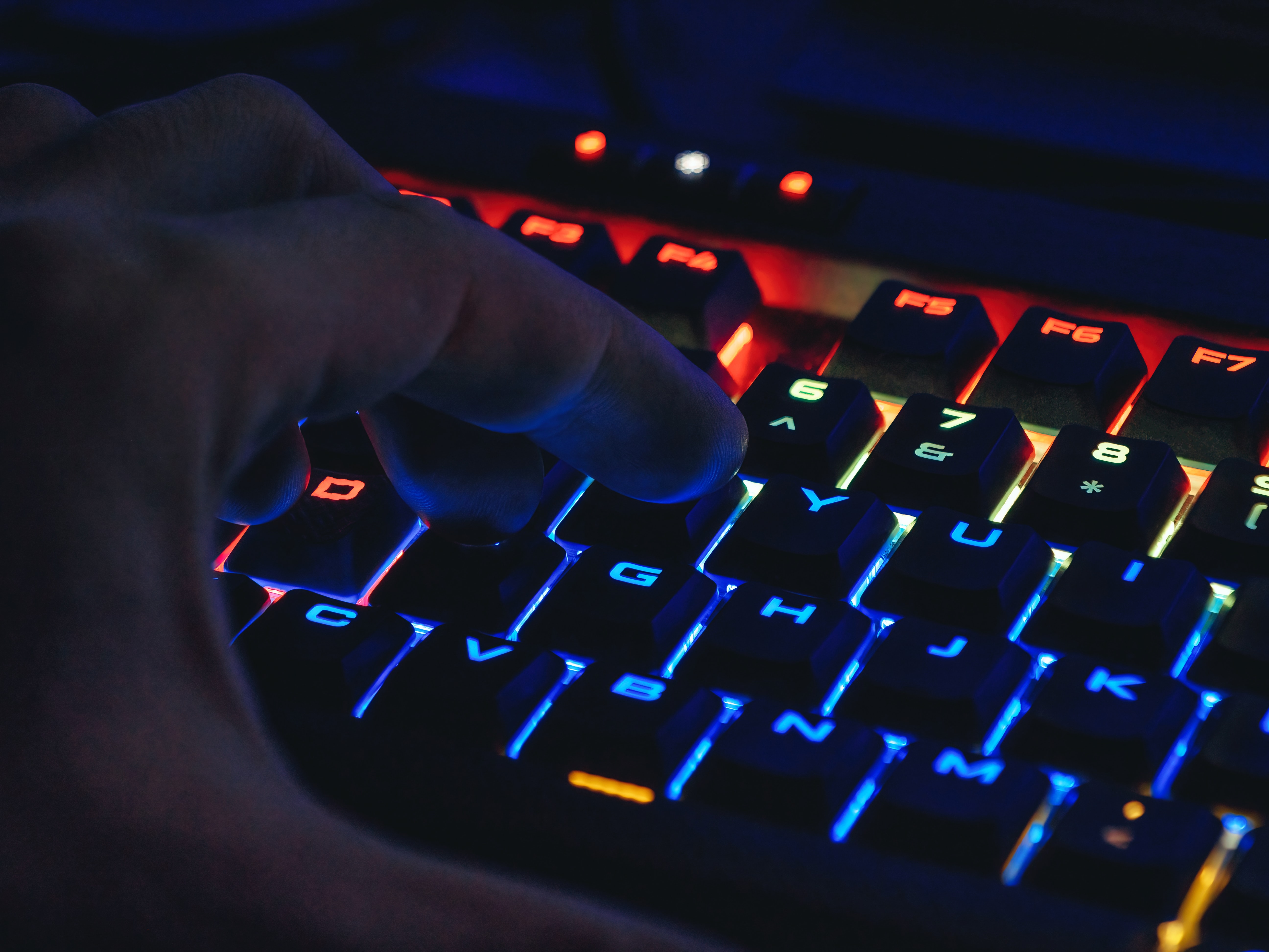 霓虹灯下的键盘闪烁着蓝色、橙色和红色。一个男人的手悬在上面，准备打字。