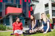 三个学生坐在哈沃顿校园花园外面，一名男性穿着红色衬衫