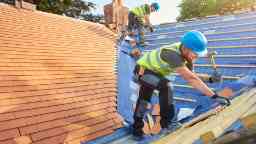 屋顶上的建筑工人安装新的屋顶瓷砖。