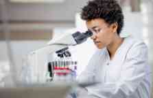 年轻的女科学家，短卷发黑发，在实验室中与显微镜一起工作，戴着白色实验室外套和塑料眼镜