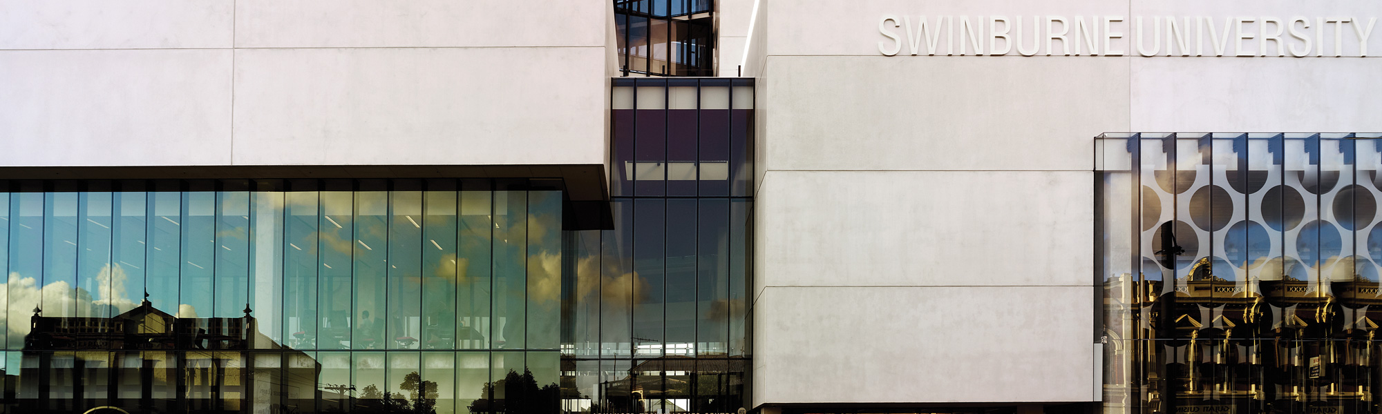 灰色的建筑立面上有斯威本大学的标志，阳光反射在窗户上。