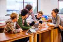 学生和他们的老师坐在一张桌子在科学实验室使用数字平板电脑。他们是caually穿着。